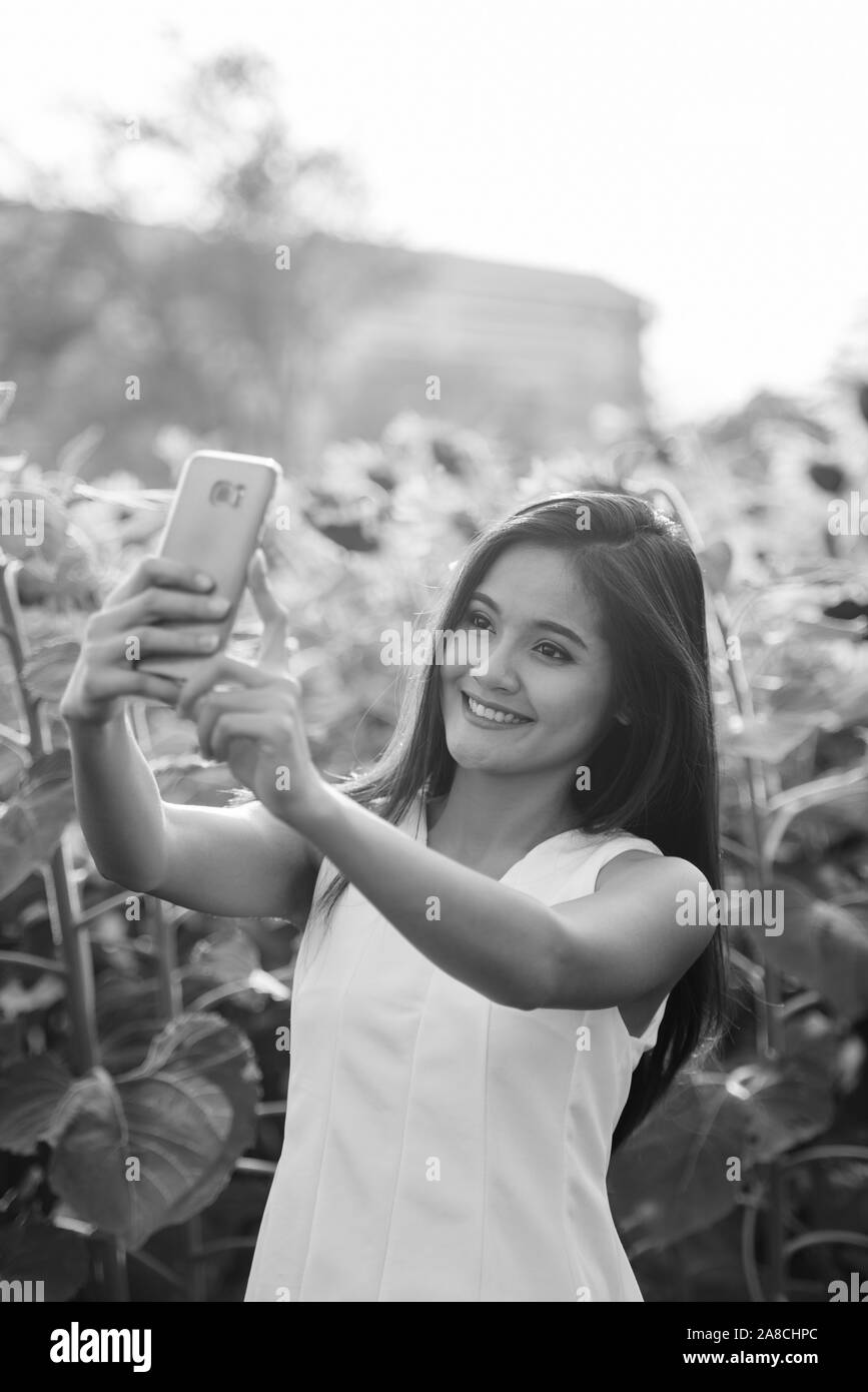 Junge asiatische Frau glücklich lächelnd während der Einnahme von selfie Bild mit Handy im Bereich der Blühende Sonnenblumen Stockfoto
