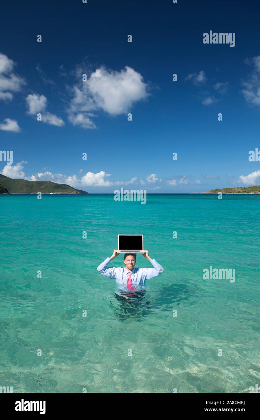 Unternehmer im Wasser balancing seinen Laptop auf seinem Kopf in hellen, blauen tropischen Meer Stockfoto