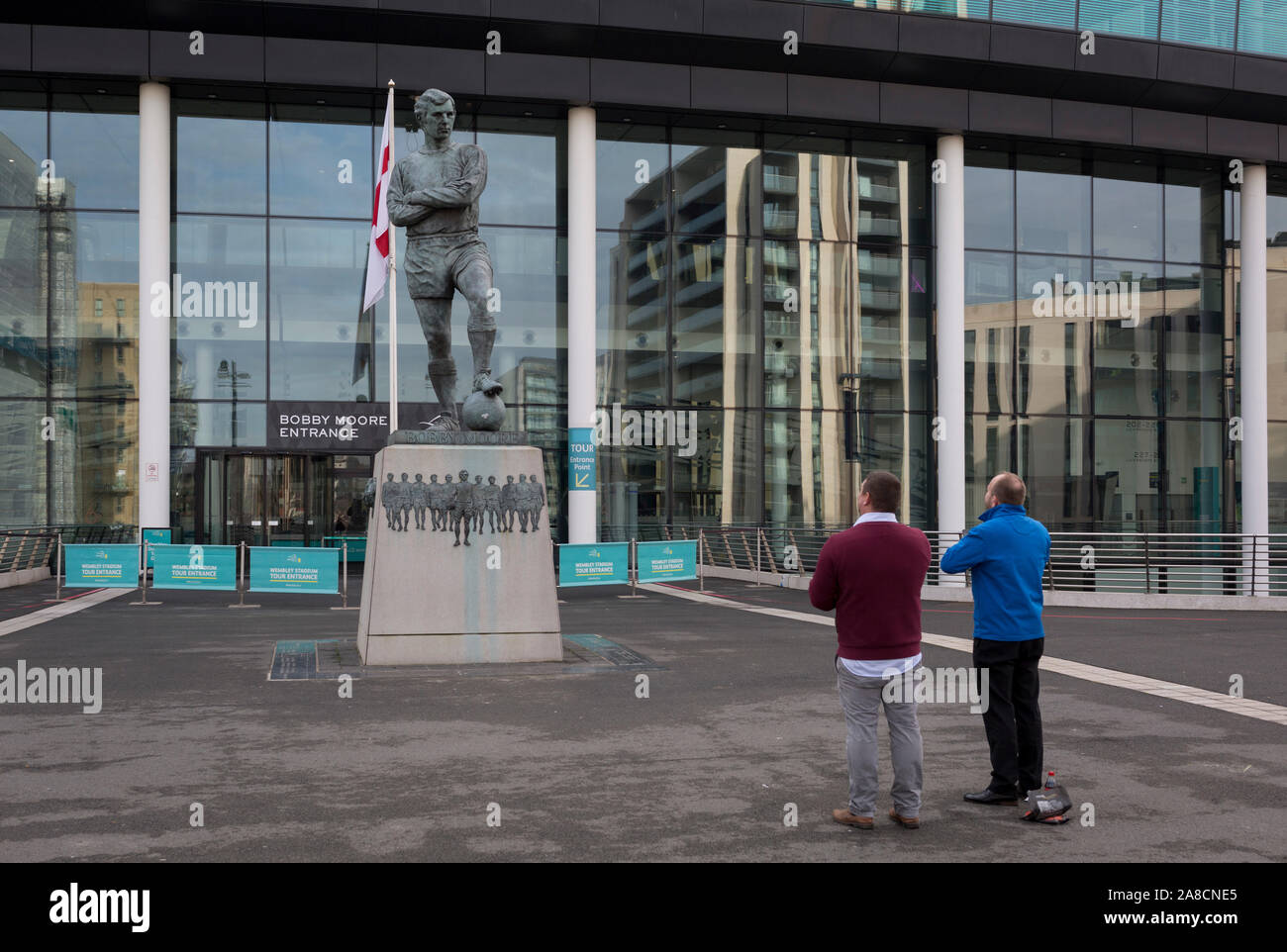 Zwei Fußball-Fans zahlen, um ihren Respekt zu der Statue des Englischen Fußball am meisten liebte Player, Bobby Moore, das am 6. November 2019, in Wembley, London, England. Sir Bobby Moore captained England zu Ihrem WM-Sieg gegen Deutschland im alten Wembley Stadion in 1966. Stockfoto