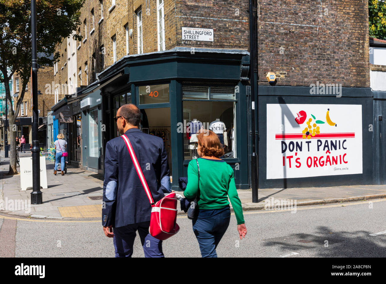 Ein paar Spaziergang, vorbei an Boutiquen und ein Wandbild mit der Meldung keine Panik Es ist organisches in Islington, London, England, UK. Stockfoto