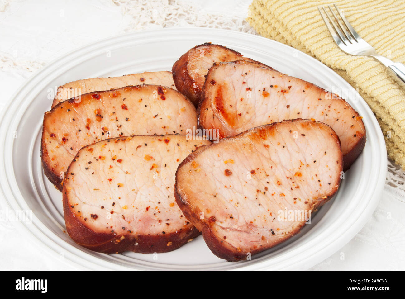 Hausgemachte Fleisch ohne Knochen geräucherte Schweinekoteletts mit verschiedenen Kräutern und Gewürzen. Eine antike Bettwäsche Tischdecke ist im Hintergrund. In natürlichem Licht gedreht. Stockfoto