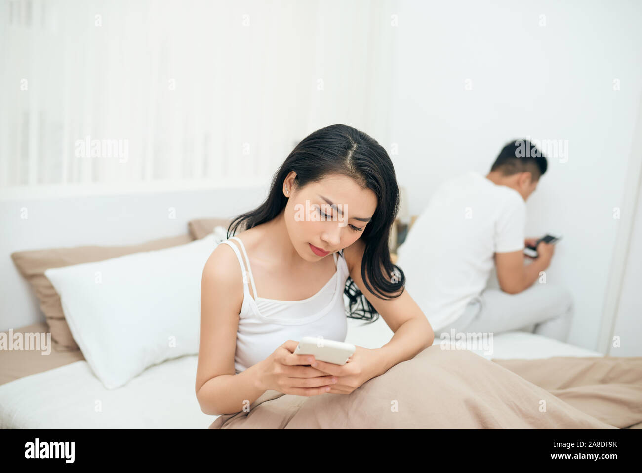 Traurige Blick auf junges Ehepaar mit ihrem Handy im Bett gegenseitig ignorieren als Fremde in Beziehung und Kommunikation Probleme Stockfoto