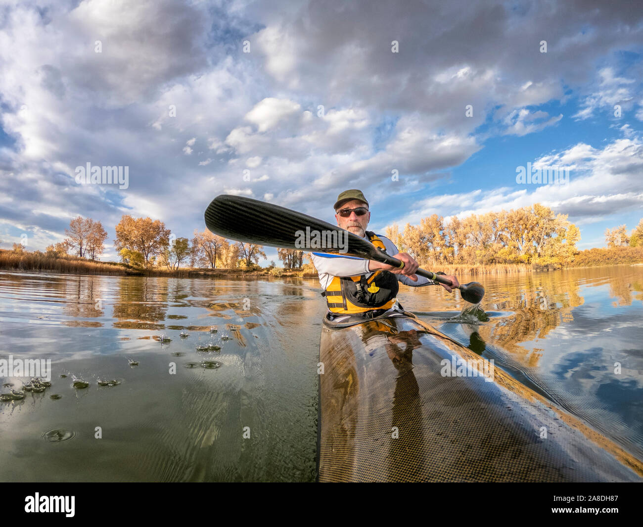 Ältere männliche Paddler ist Paddeln eine lange, schmale und schnelle racing Sea Kayak auf einem ruhigen See, Herbst Landschaft in Colorado, POV aus einer Aktion Kamera - outdoo Stockfoto