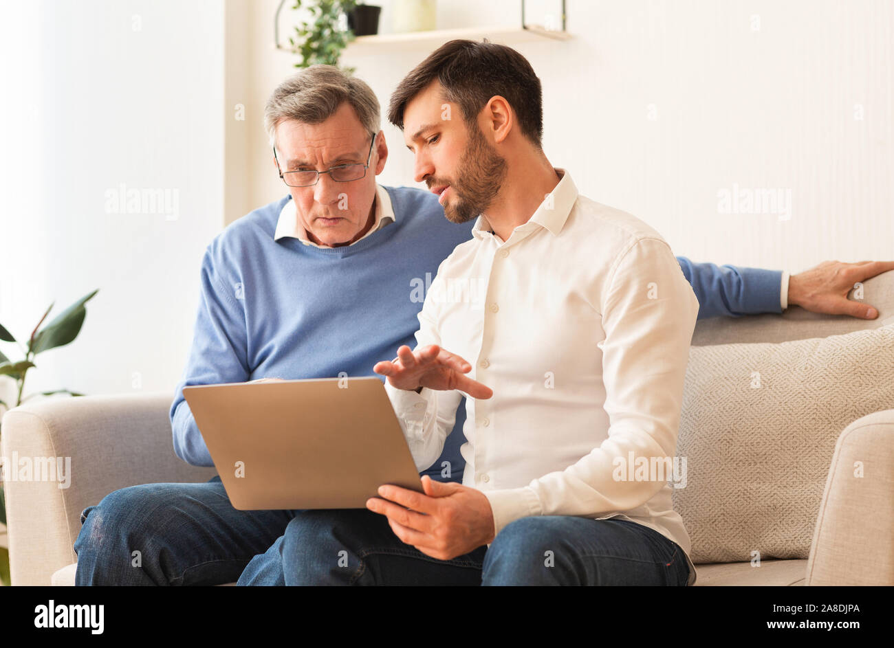 Middle-Aged Sohn Lehre Vater Setzen Laptop Indoor Stockfoto