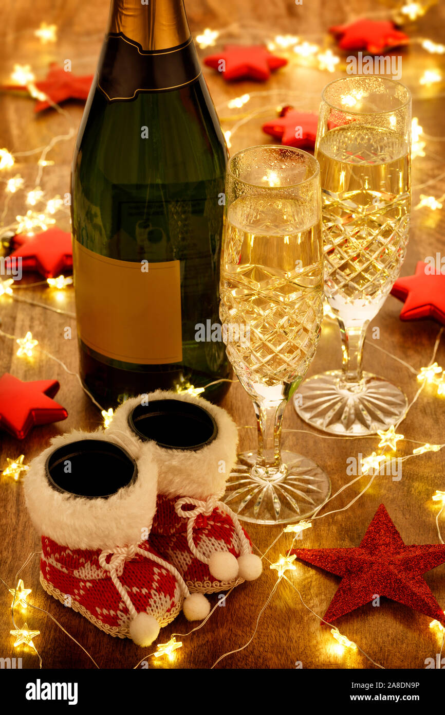 Champagnergläser und Flasche mit Weihnachtsbeleuchtung, Kugeln und roten Sternen Dekorationen, auf einem Holztisch Stockfoto