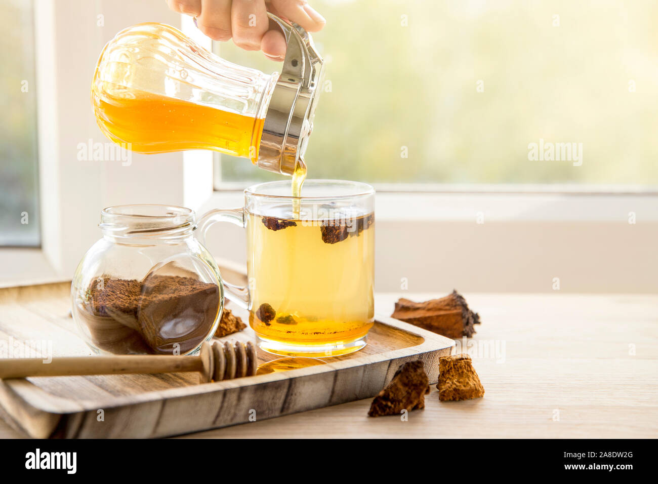 Gesunde reine wild natürliche chaga Pilz aus Birke, Inonotus obliquus Stücke in Kaffee Glas auf Holz- Fach auf der Fensterbank, schöne sonnige zurück Licht. Stockfoto