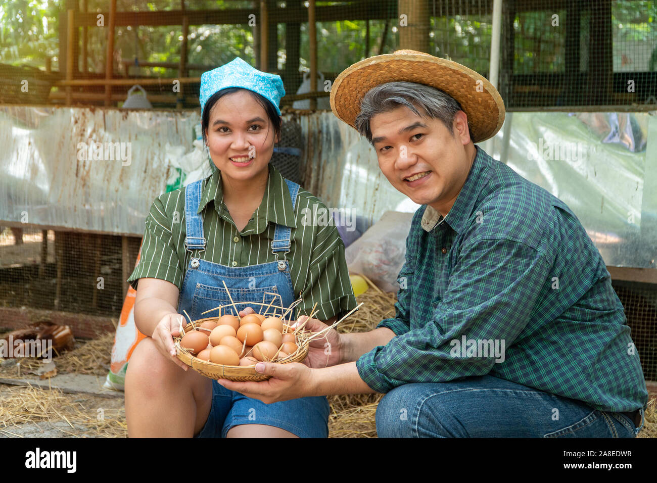 Asiatische paar Bauer Holding frisches Huhn Eier in Korb saß in der Nähe von Henne neben Hühnerfarm. Lächeln, weil mit den Produkten zufrieden aus der f Stockfoto