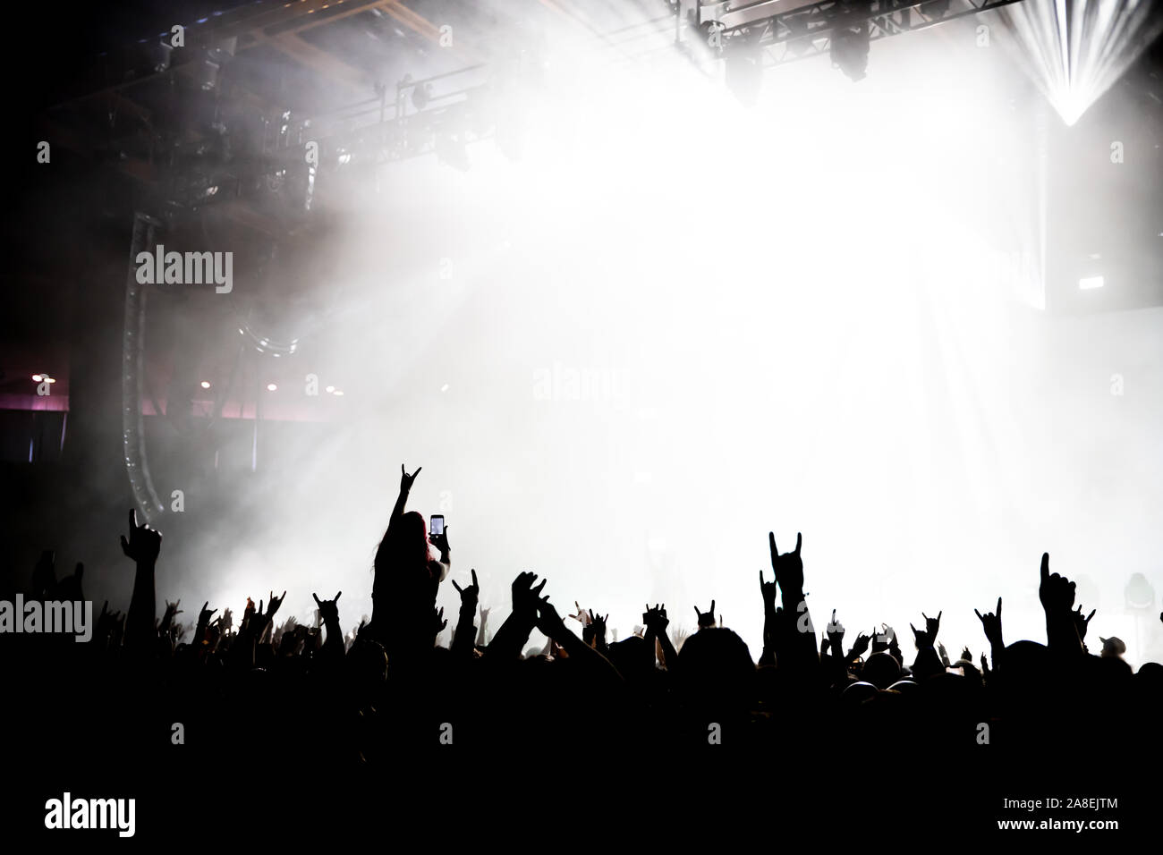 Eine Silhouette von Fans für eine Band, die auf der Bühne nicht mehr erkennbar ist, von der Bühne aus Licht und Nebel. Stockfoto