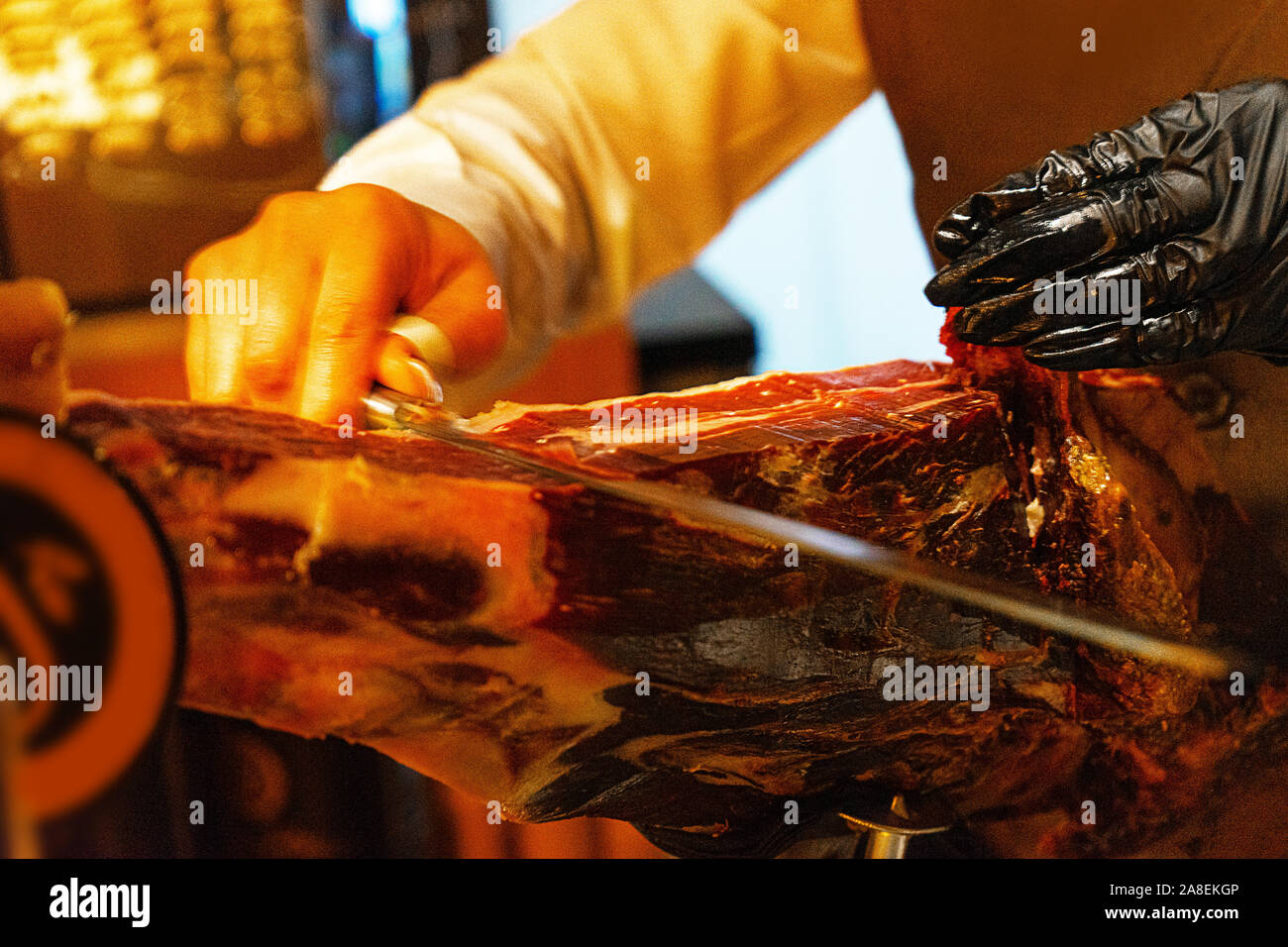 Hände einer Frau in Schwarz Handschuhe schneiden Sie ein Stück vom traditionell spanischen Jamón de Bellota im Restaurant oder Markt- bzw. speichern. Fleisch Nahaufnahme. Selektive konzentrieren. Stockfoto