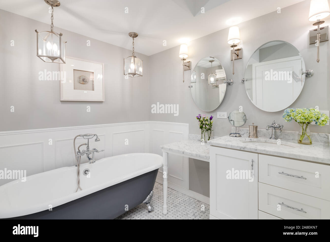 Eine schöne, weiße Badezimmer mit einem Stand alone clawfoot Badewanne mit Chrom Hardware. Blumen auf dem weißen Marmor Zähler nach oben. Stockfoto