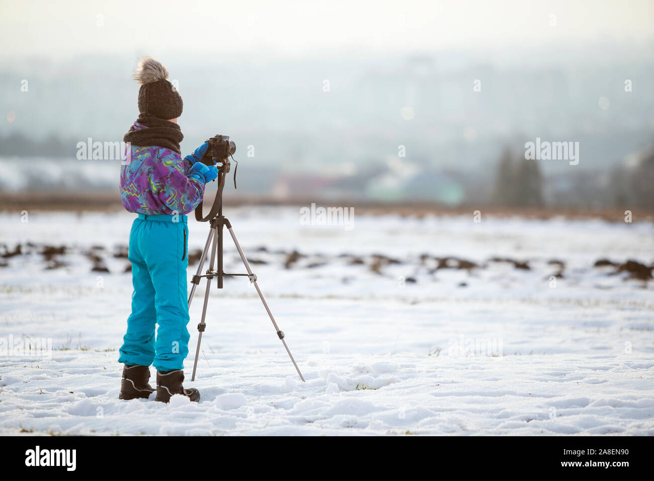 Kind Junge Fotografieren im Winter draußen mit Foto Kamera auf einem Stativ auf schneebedeckten Feld. Stockfoto