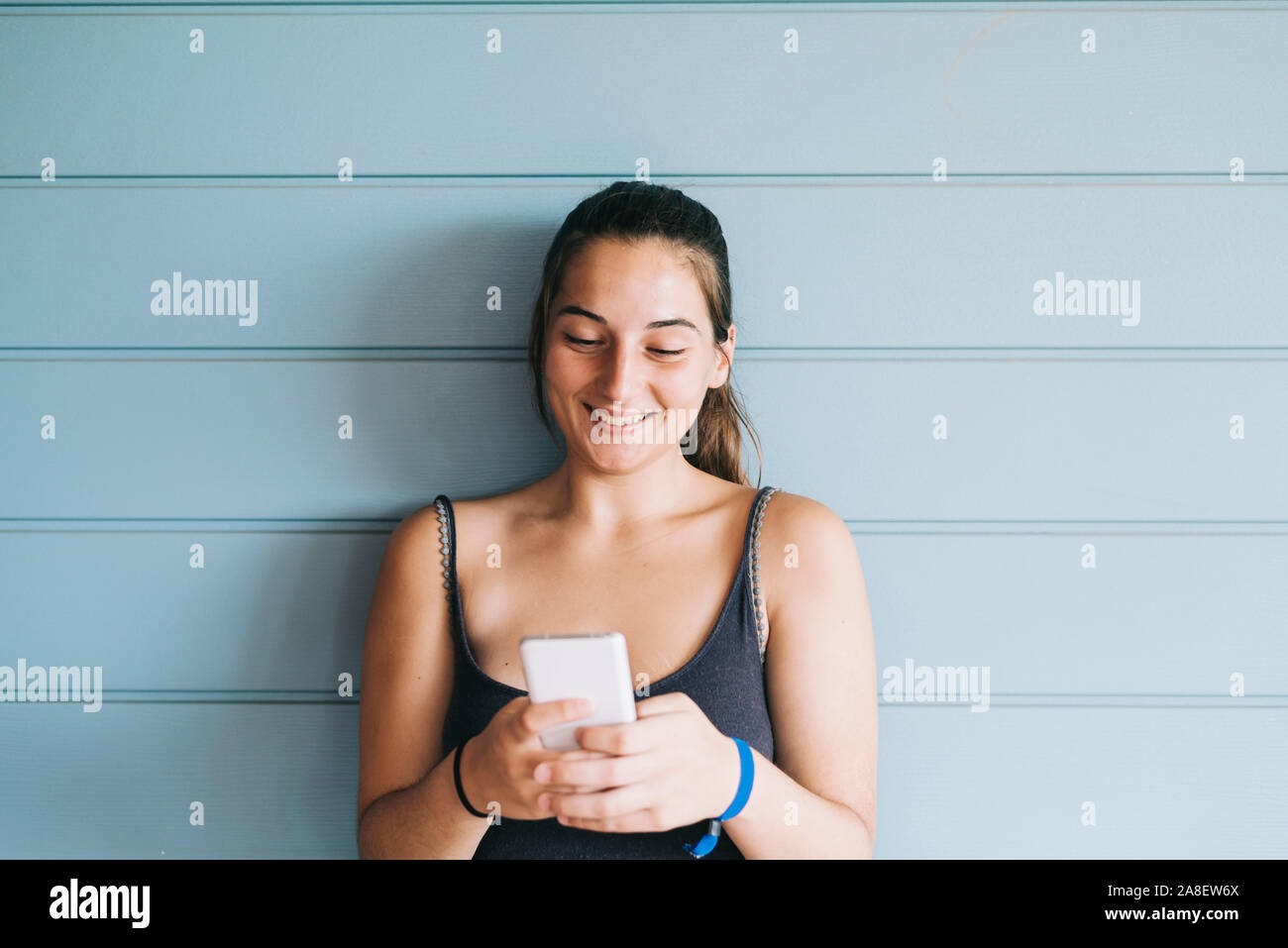Schöne Frau lehnte sich auf einem Holz Wand, während mit einem Smartphone Stockfoto