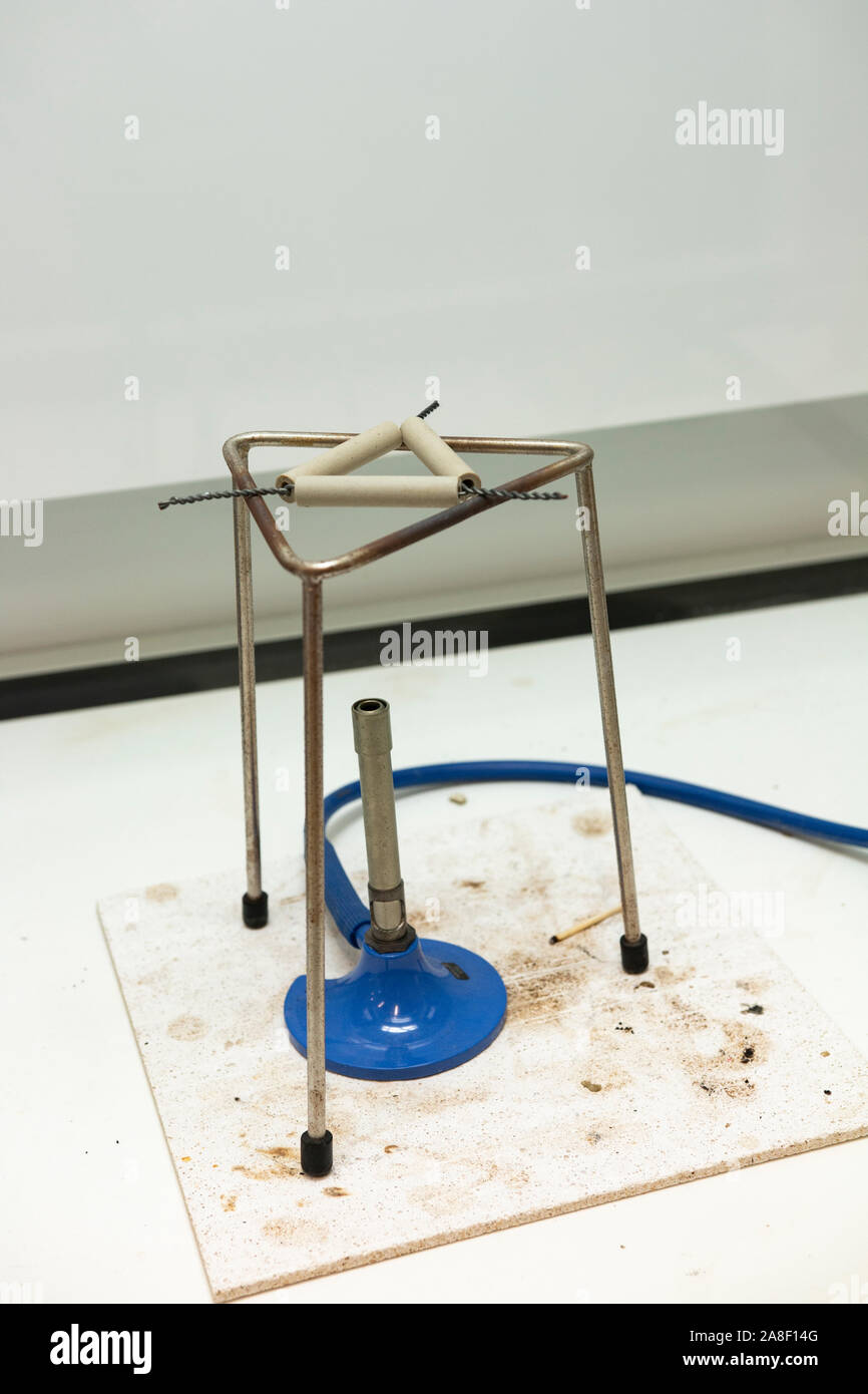 Bunsenbrenner mit Stativ und Leitung Ton Dreieck in einem Labor workbench in Großbritannien, beleuchtet mit einem warmen und vollen Flamme Stockfoto