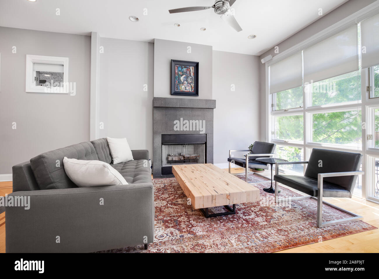 Ein luxuriöses Wohnzimmer mit schwarzen Ledersesseln, komfortable grau Couch mit weißen Akzenten Kissen, Holz Couchtisch und einem Kamin an der Wand. Stockfoto