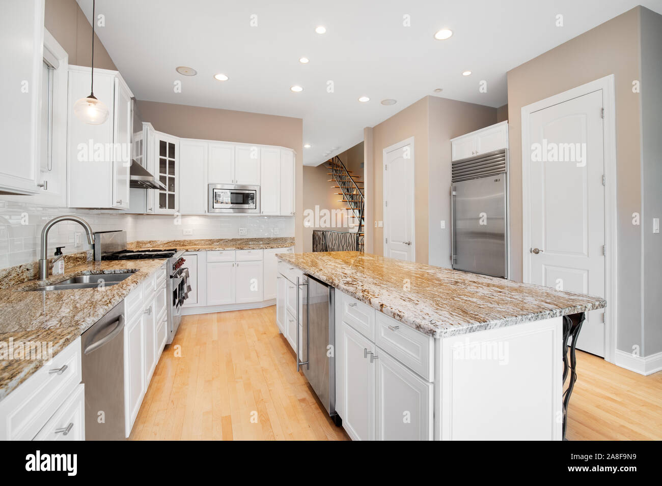 Eine große weiße Küche in einem luxuriösen Haus mit Holzböden, Küchengeräte aus Edelstahl, Granit und weißen Schränke. Stockfoto