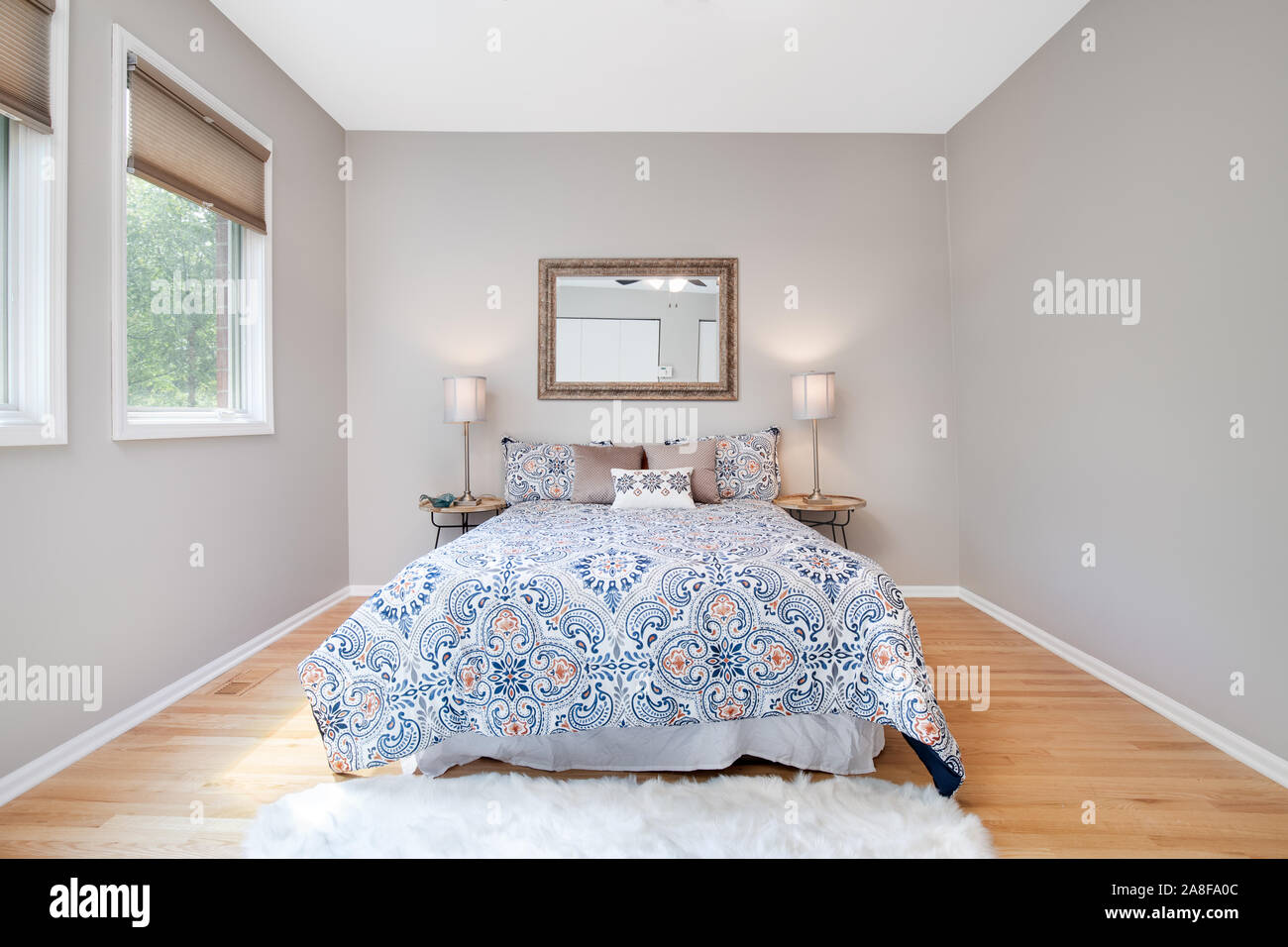 Ein Bett im Schlafzimmer zu einer Residenz zentriert mit zwei Lampen auf dem Nachttisch und ein Spiegel hängt über dem Bett. Stockfoto