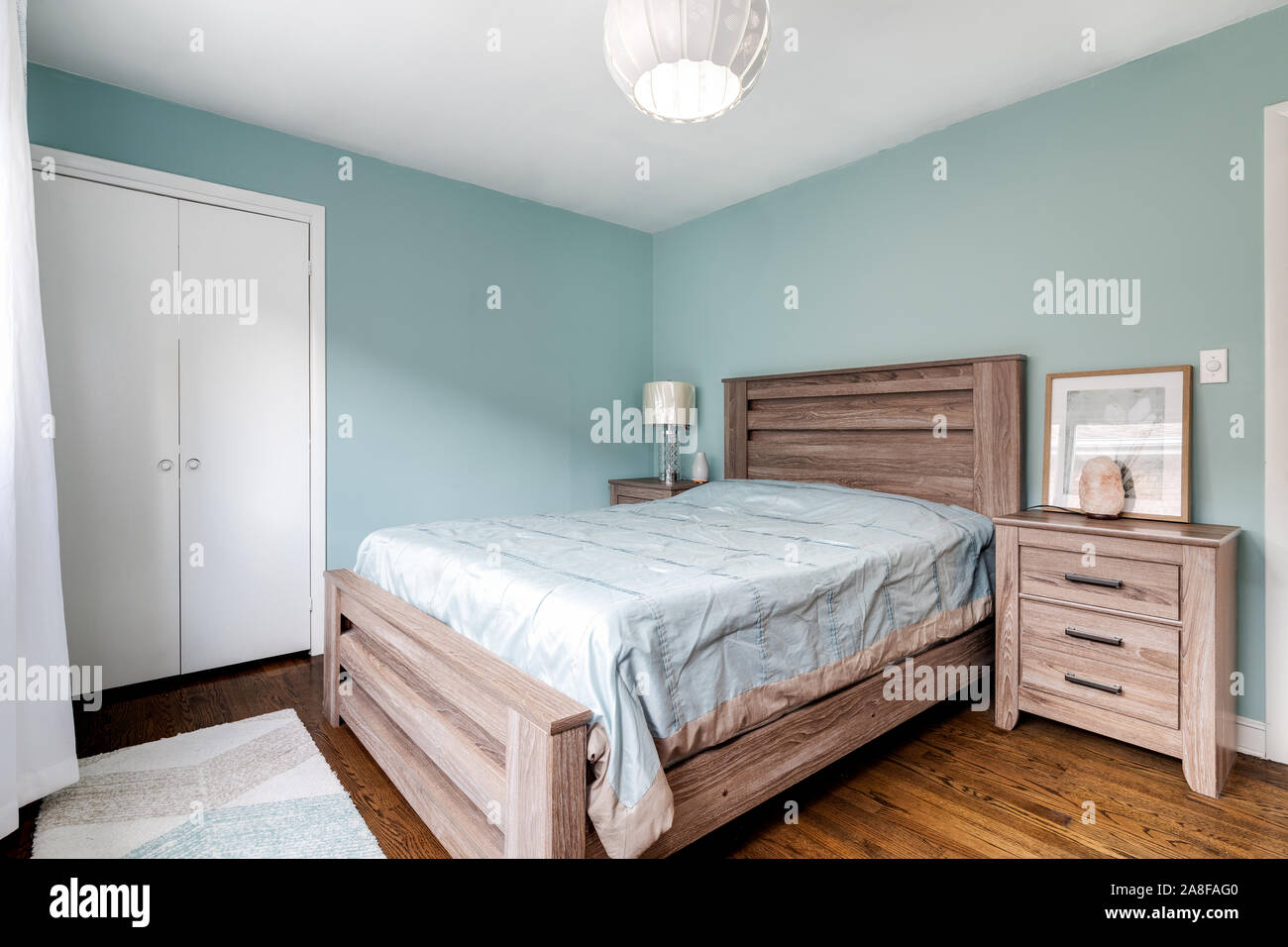 Ein kleines Schlafzimmer mit einem hellen Schlafzimmer möbel, türkisfarbenen Wänden, Holzböden und ein schickes Licht hängen. Stockfoto