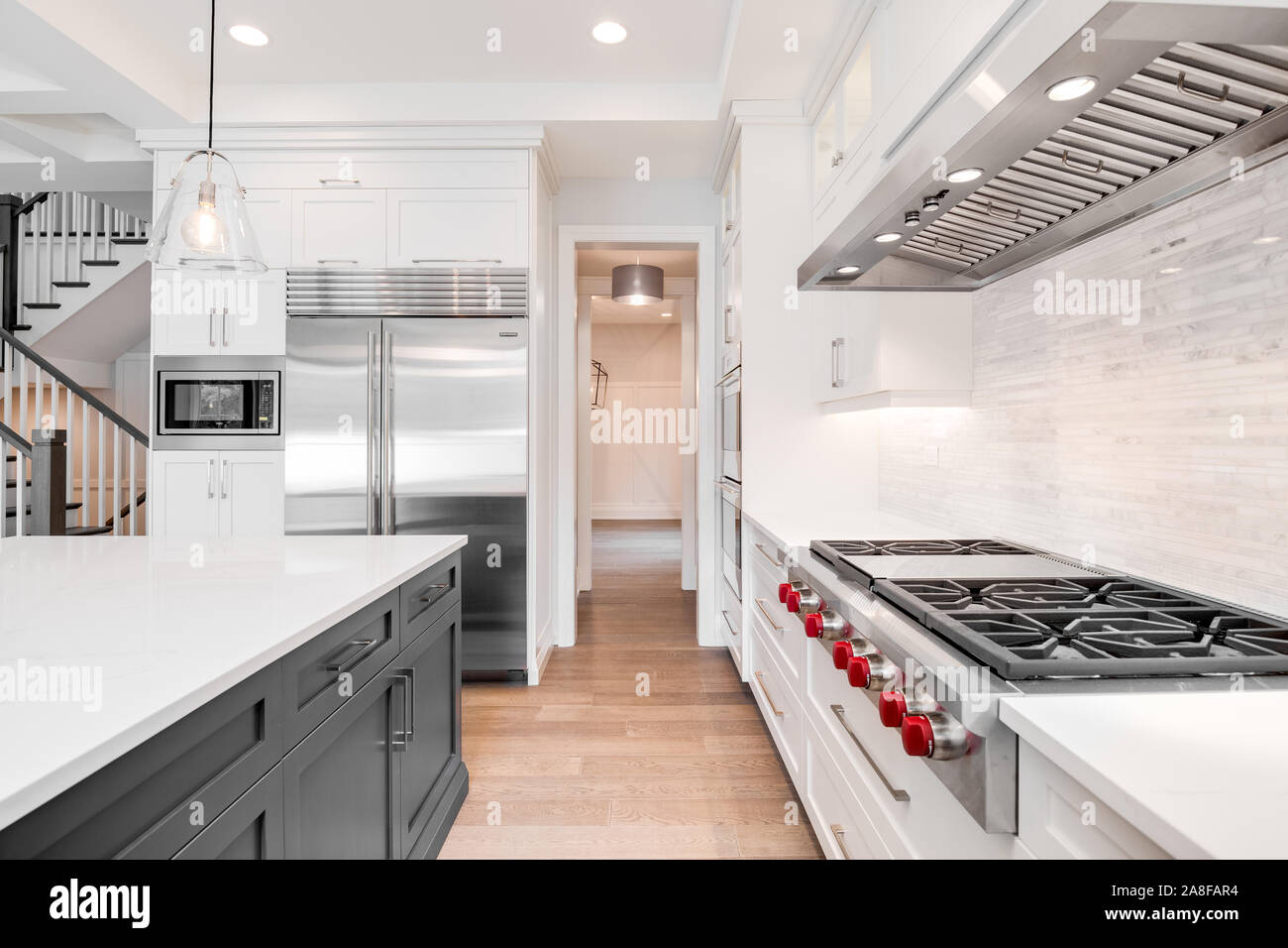 Eine luxuriöse, moderne Küche mit Edelstahl Wolf Geräte durch weißen Schränke, schöne Granit umgeben, und Massivholzböden. Stockfoto