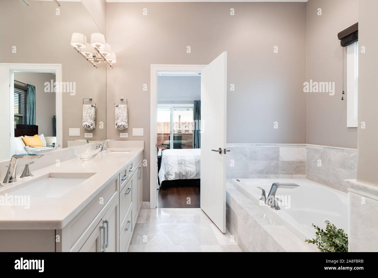 Ein luxuriöses Badezimmer mit einer Badewanne und einem hellen Doppelwaschtisch in Richtung Schlafzimmer. Stockfoto