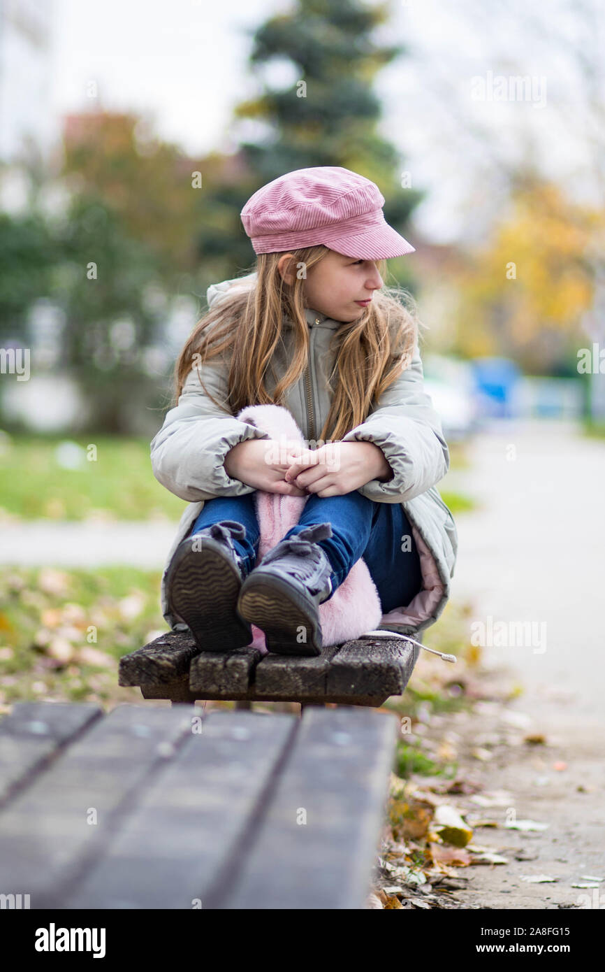 Süße kleine Mädchen imaginären auf der Bank im Park im Herbst kühlen Tag sitzen. Mädchen in rosa Hut. Herbst Wetter. Stockfoto