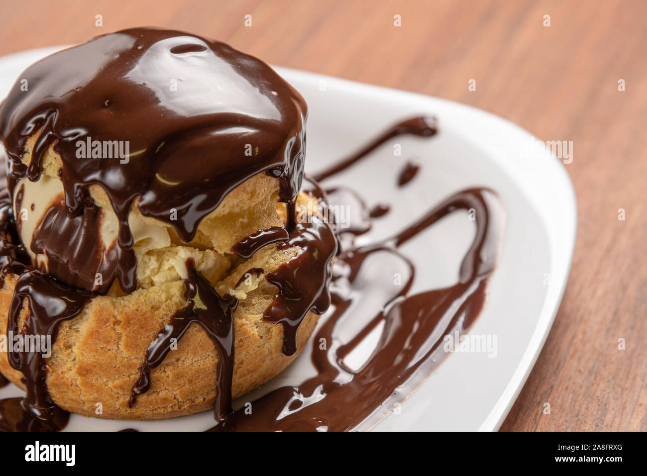 Windbeutel mit Eis und Schokolade. Eclairs mit schwarzer Schokolade auf ...