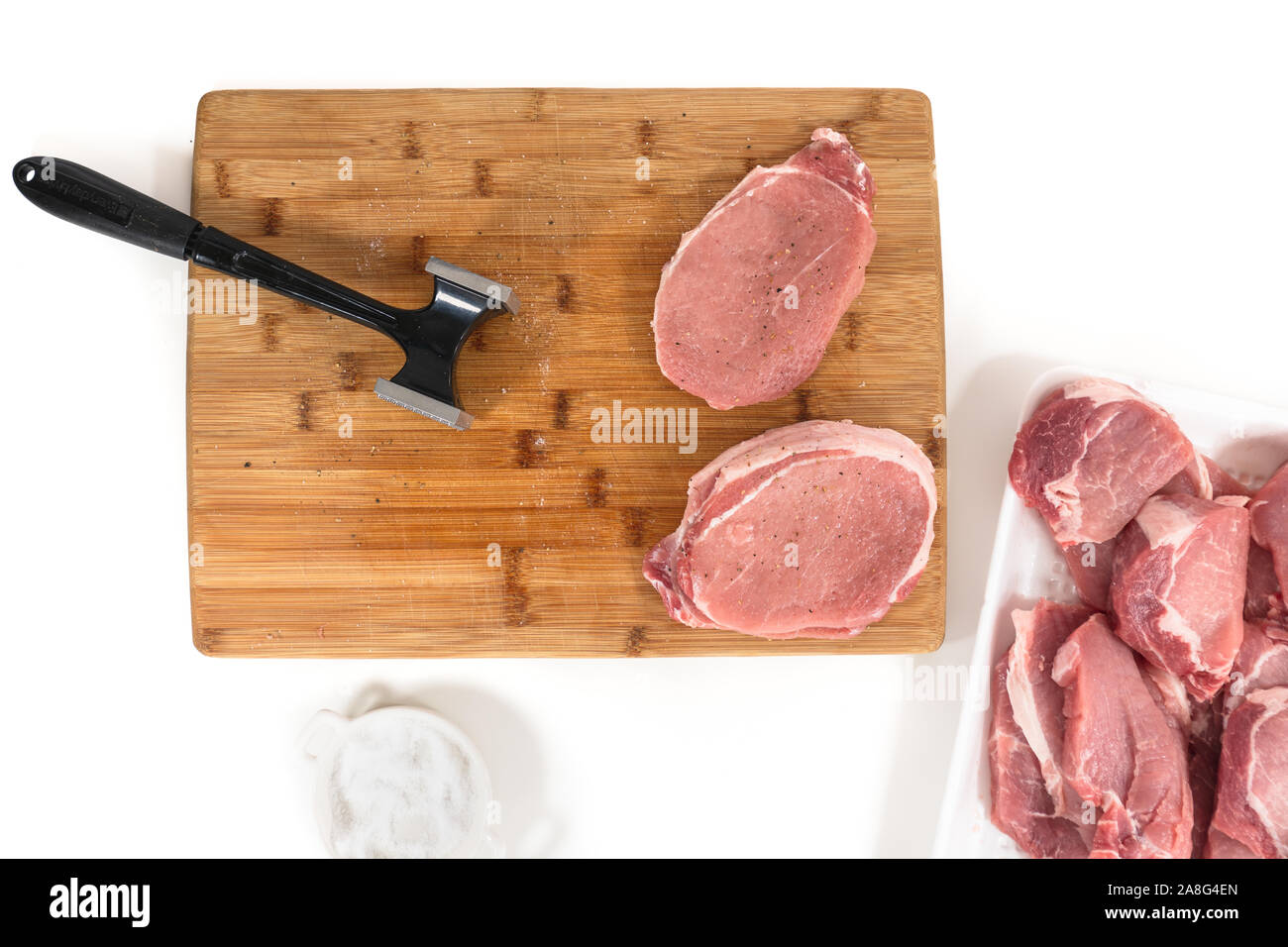 Rohes Schweinefleisch ohne Knochen Kotelett Koteletts und meat Tenderizer [auf einer hölzernen Schneidebrett, Nahaufnahme, direkt von oben, auf weißem Hintergrund Stockfoto