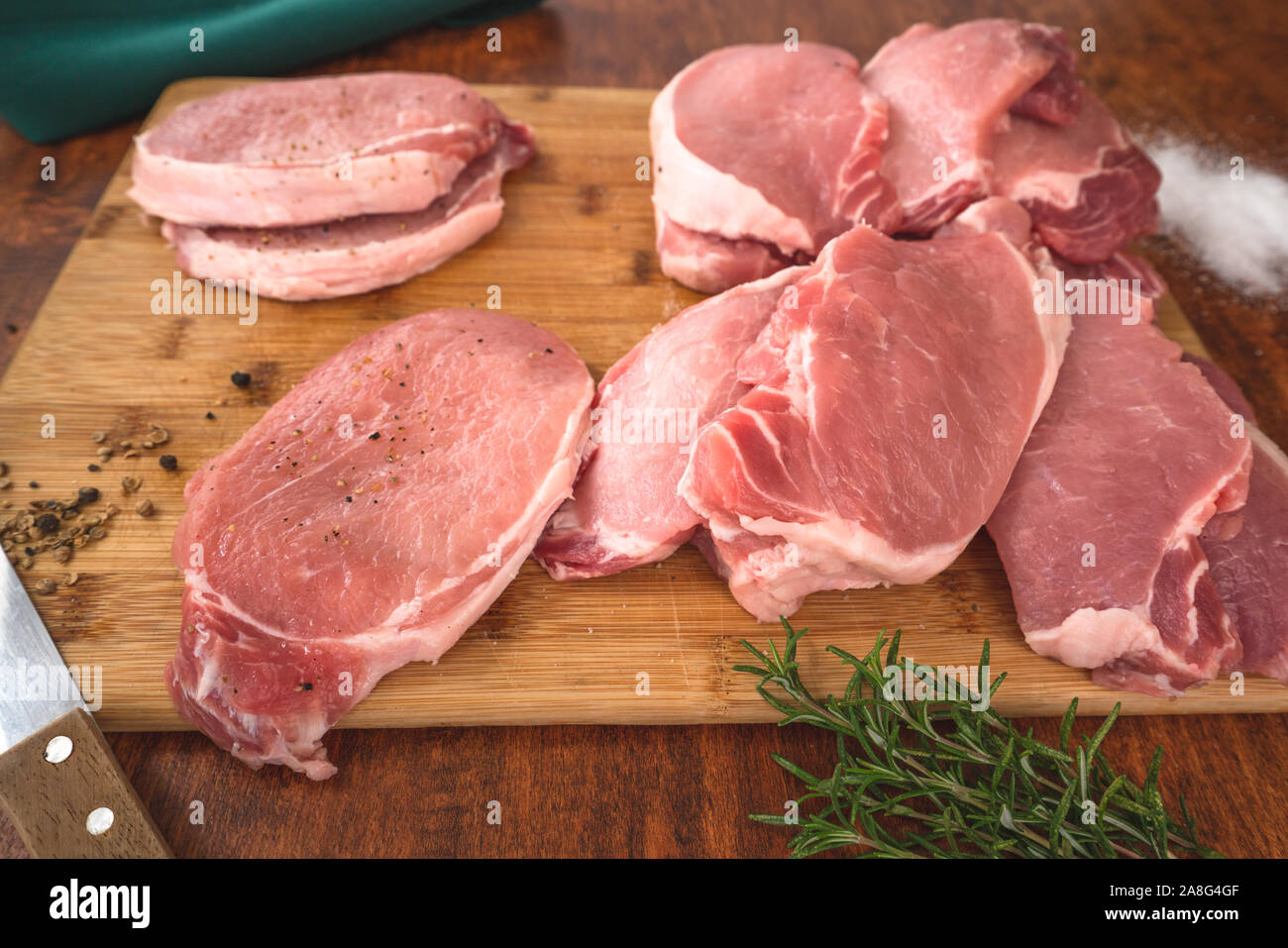 Rohes Schweinefleisch ohne Knochen Kotelett Koteletts auf Holz Schneidebrett mit einige Kräuter, Salz und Rosmarin in der Nähe auf einem Holz- rustikalen Hintergrund Stockfoto