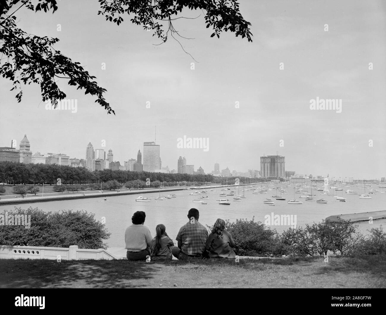 Eine Familie sitzt das Shedd Aquarium entlang Solidarität Drive mit Blick auf den Chicago Monroe Harbour und die northside Skyline, Ca. 1960. Stockfoto