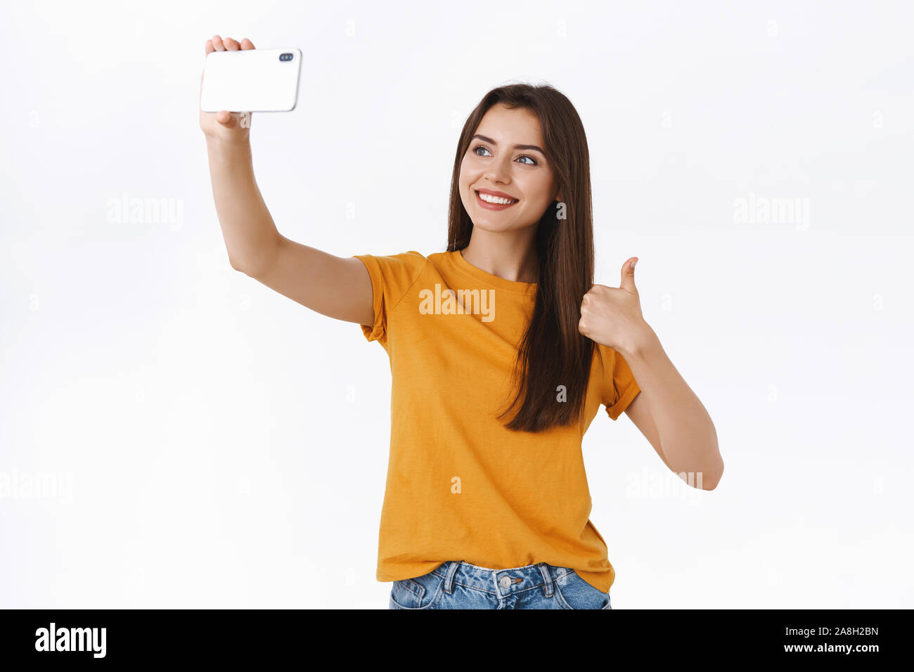 Upbeat, gut aussehende Fröhliche brünette Frau im gelben T-Shirt, Datensatz vlog oder in der Nähe von selfie Tolle oder Shop, Zeige Thumbs-up lächelnd Stockfoto