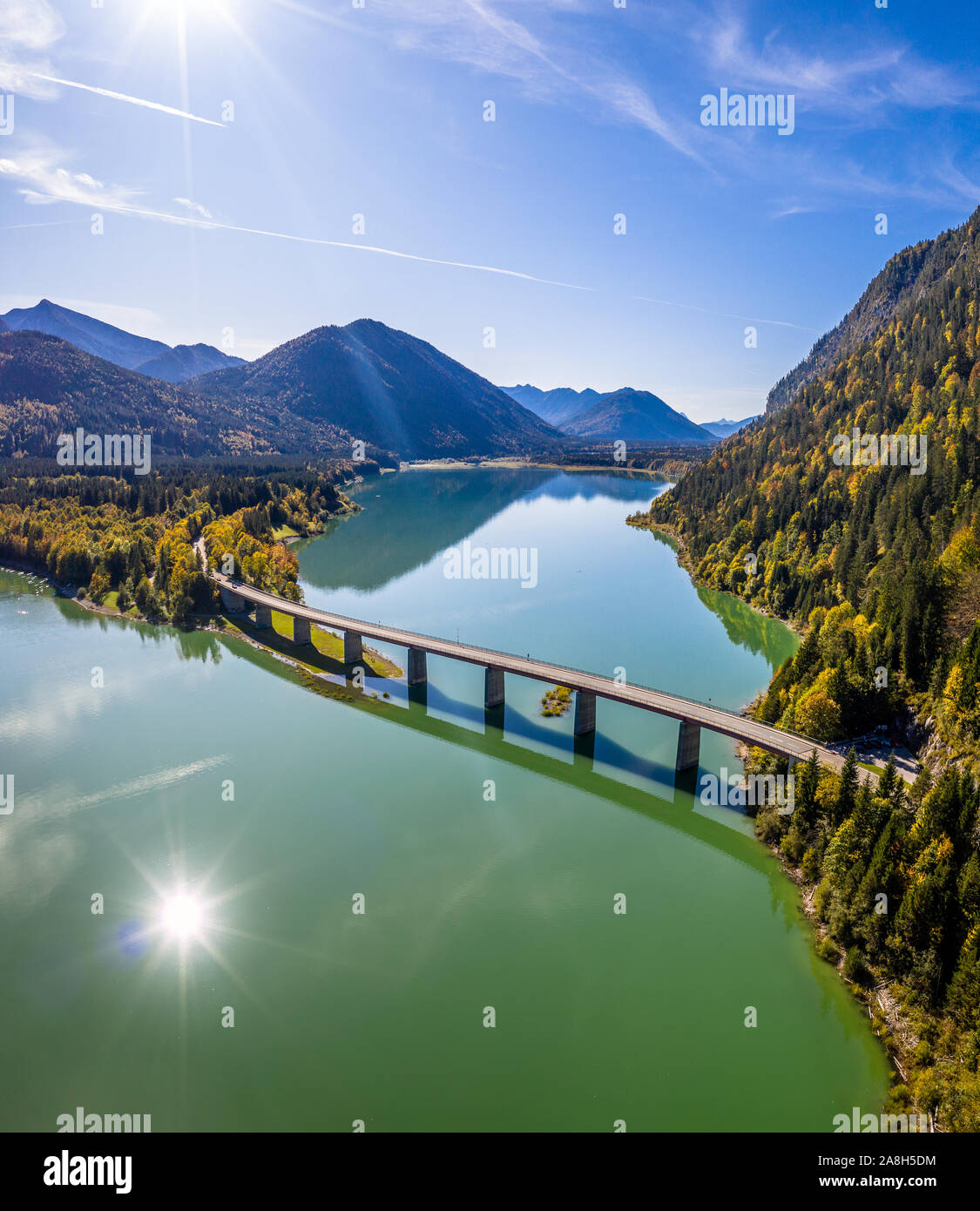 Malerische Luftaufnahme der Brücke über den See Sylvenstein mit schönen Reflexionen. Alpen Karwendelgebirge im Rücken. Herbst Landschaft von Bayern Stockfoto