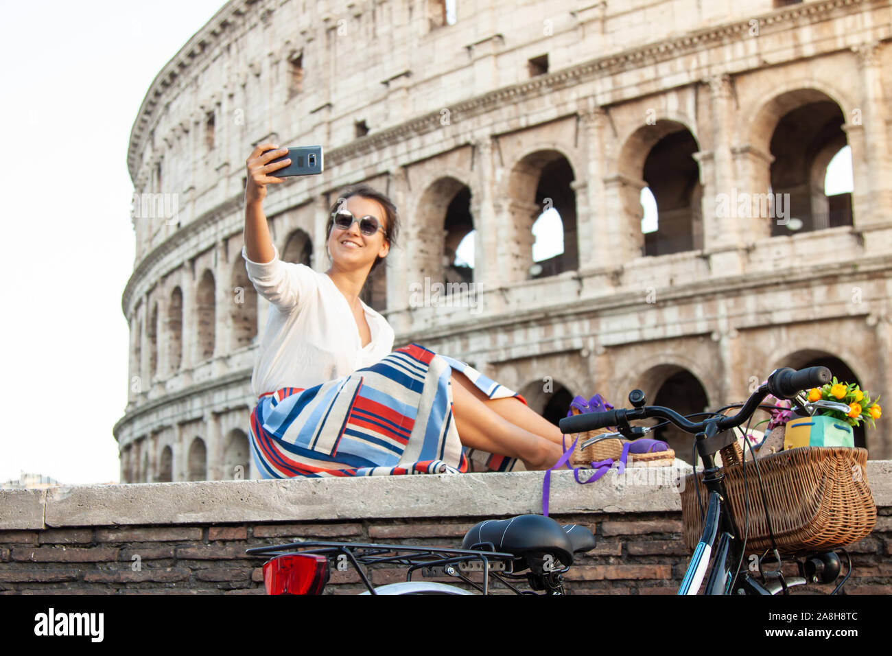 Schöne junge Frau unter selfie Bilder mit Smartphone sitzen vor dem Kolosseum in Rom bei Sonnenuntergang. Stockfoto