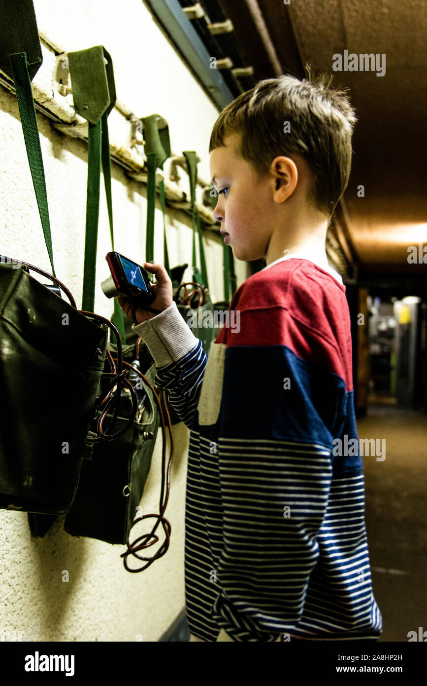 Ein Junge nimmt Bilder im Kelvedon Hatch secret Nuclear Bunker Eingang Tunnel. Altmodische Säcke und Radios an der Wand Stockfoto