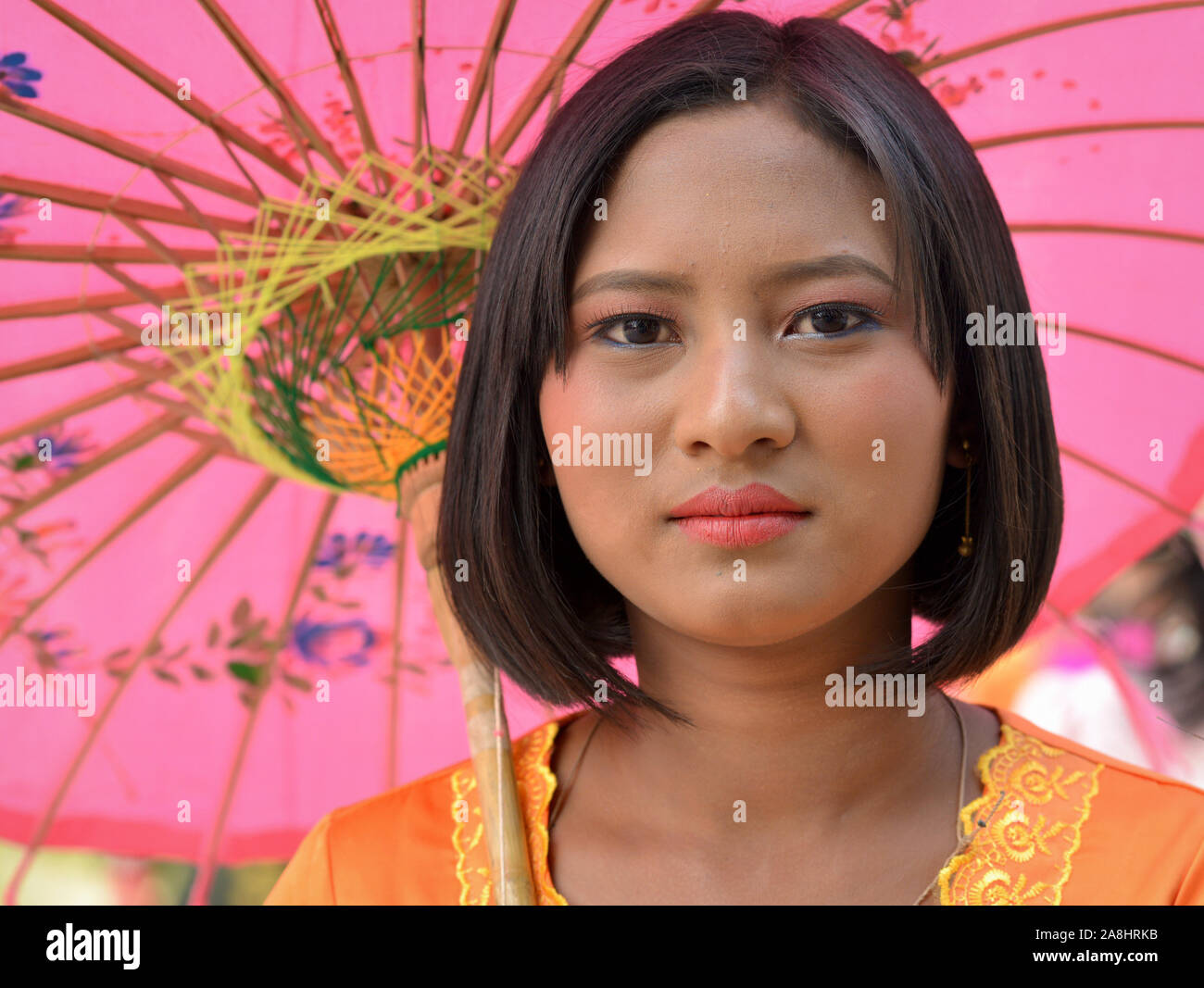 Die burmesische Mädchen hält einen farbenfrohen traditionellen Papier Sonnenschirm und posiert für die Kamera während eines traditionellen buddhistischen Feier. Stockfoto