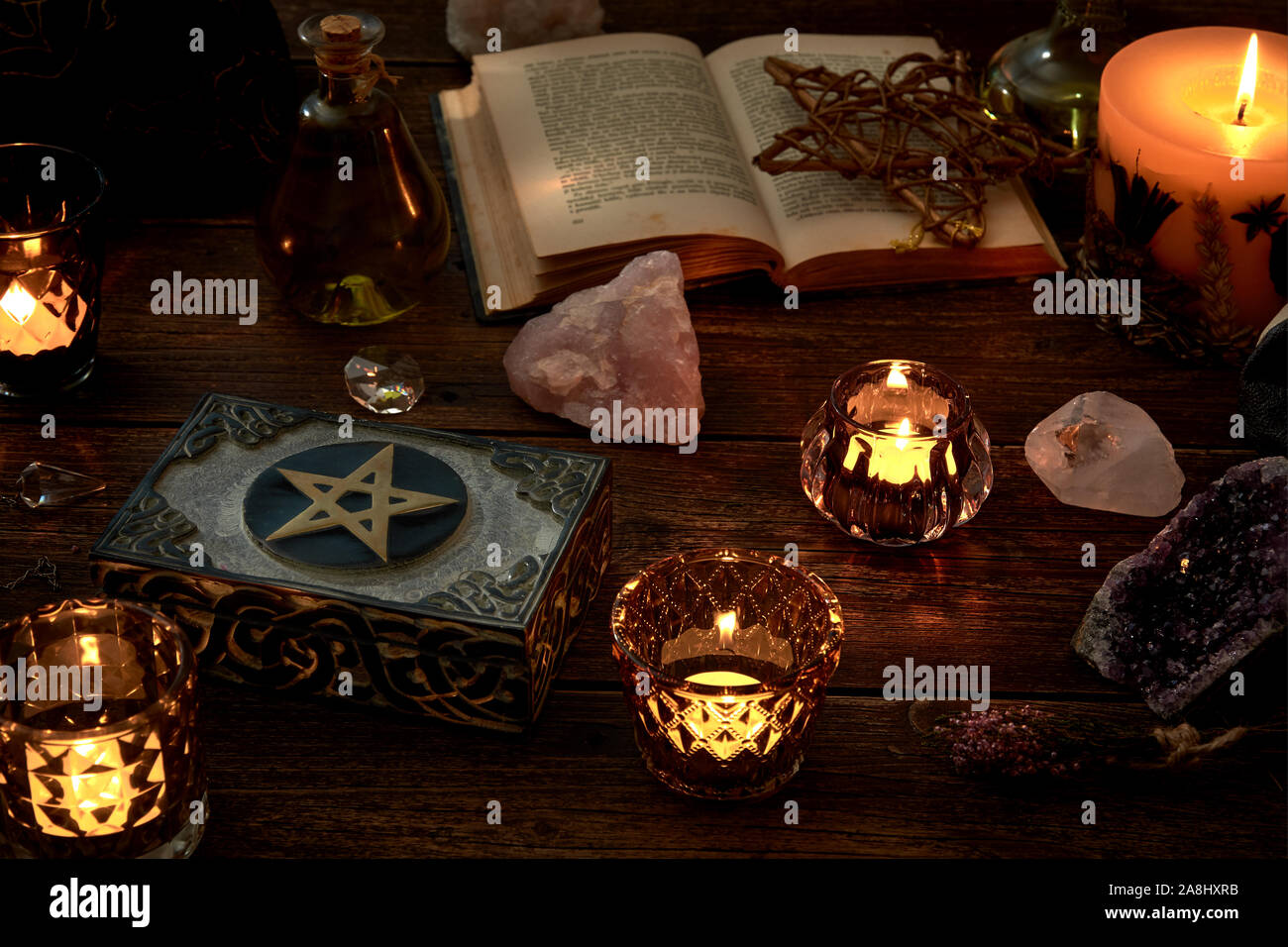 Esoterische oder mystische Stillleben mit einer Kiste und ein paar brennende Kerzen, ein pentagramm Neben ein offenes Buch. Pendel und Edelsteine auf alte, Registerkarte Stockfoto
