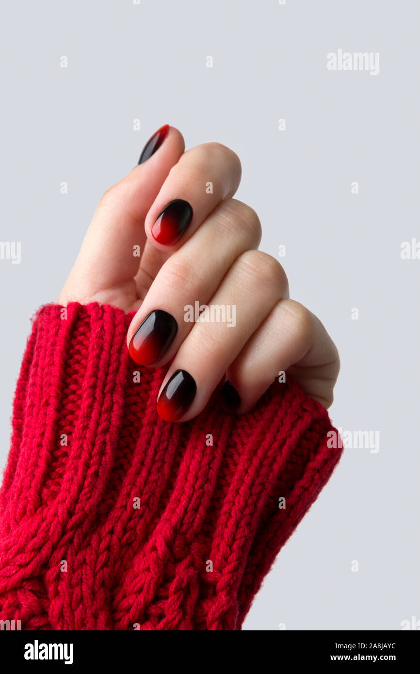 Weibliche hand mit Rot Schwarz ombre gradient Nägel in Pullover Stockfoto