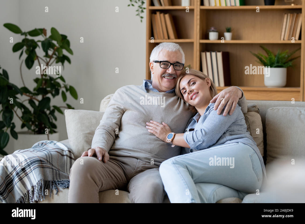 Fröhliche Frau mittleren Alters in der casualwear Biegen zu Ihrem älteren Vater Schulter Stockfoto