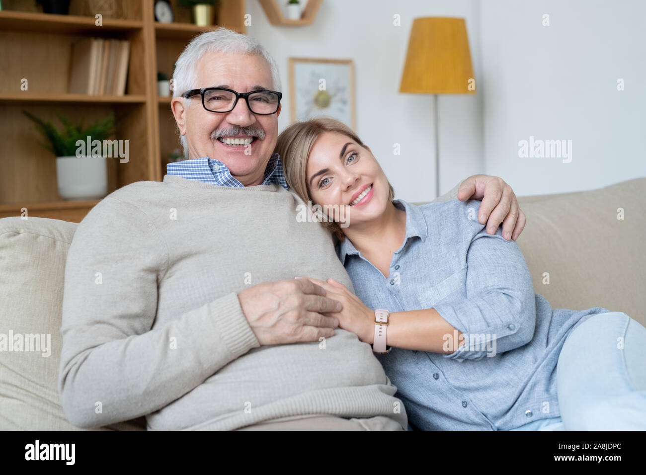 Hübsche junge lächelnde Frau und ihr glückliches senior Vater entspannt auf der Couch zu Hause Stockfoto