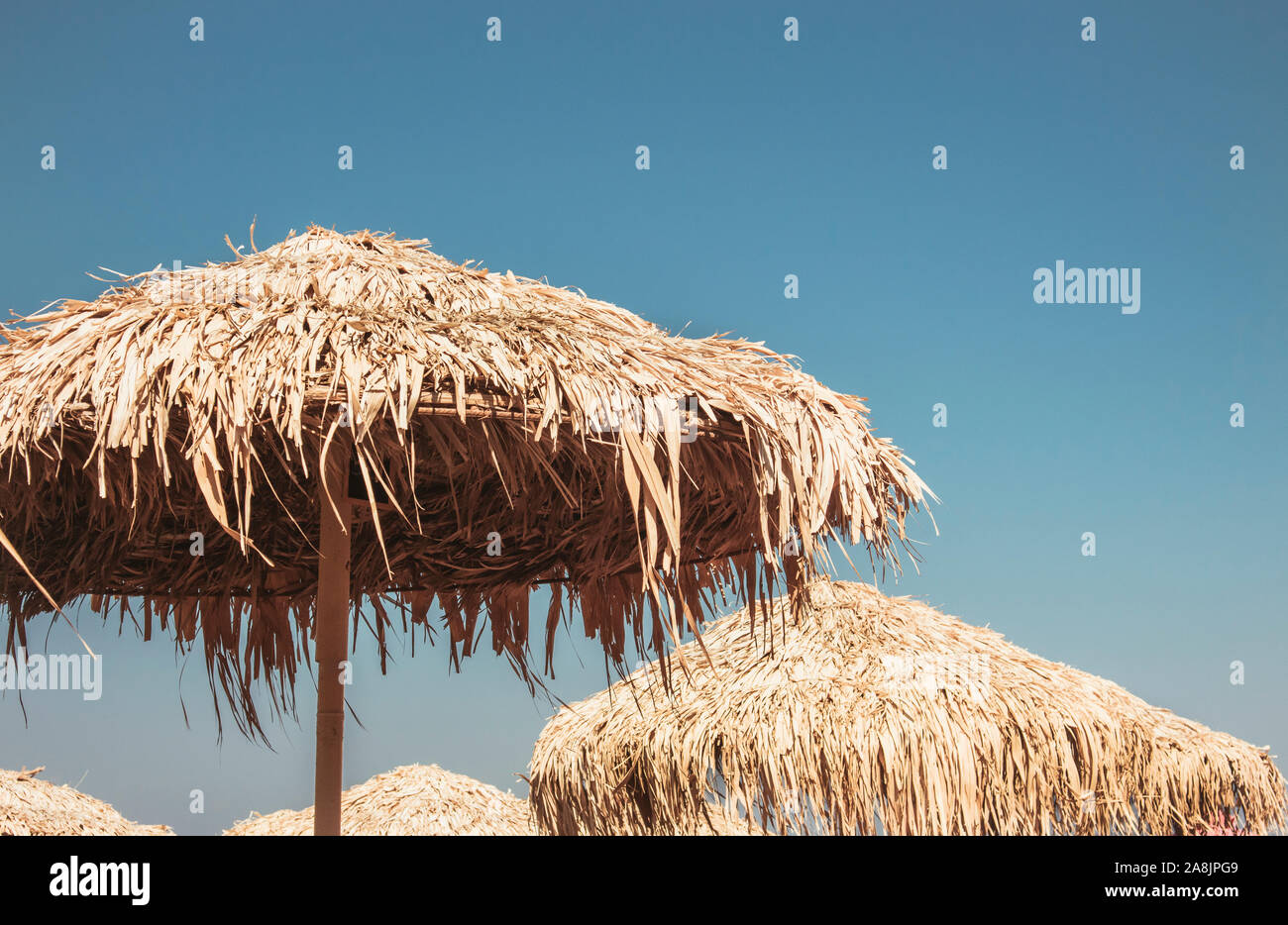 Blick über Vintage Stroh Sonnenschirme gegen blauen Himmel. Entspannender Sommerurlaub Konzept, Hintergrund mit Kopierraum. Stockfoto