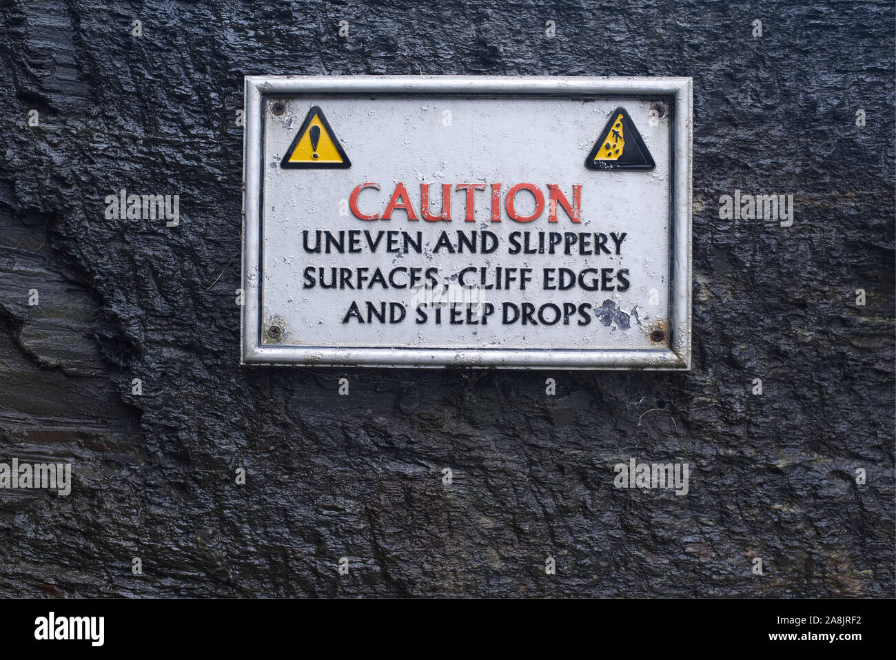 Vorsicht uneben und rutschig, Klippen und steilen Tropfen Oberfläche Schild schwarze und gelbe Warndreieck mit Mann rutscht, die nassen Felsen Hintergrund Stockfoto