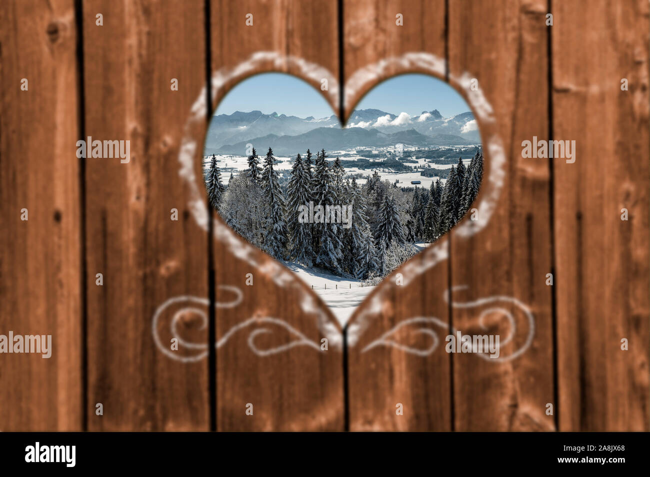Auf der Suche durch eine geschnitzte Herz in eine Holzwand zu wunderschönen verschneiten Landschaft Stockfoto