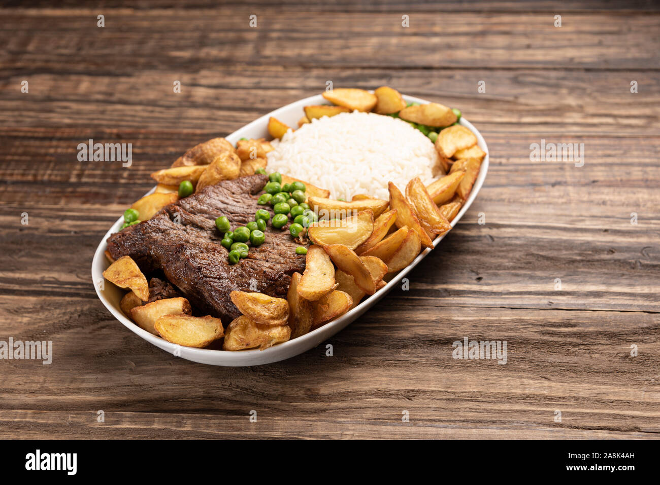 Rindersteak mit rustikalen Kartoffel- und ricei auf Holztisch, Hintergrund, weiches Licht Stockfoto