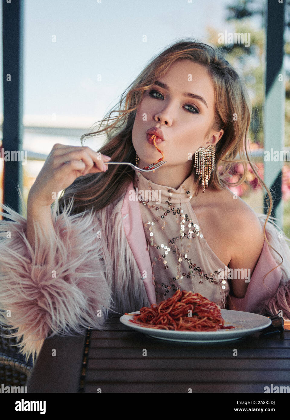 Süße Mädchen in einem Restaurant sitzen und essen Nudeln (Spaghetti). Portrait von stilvollen junge Frau im Cafe, das Tragen von Kleidung und Pelzmantel. Filmkorn Wirkung Stockfoto