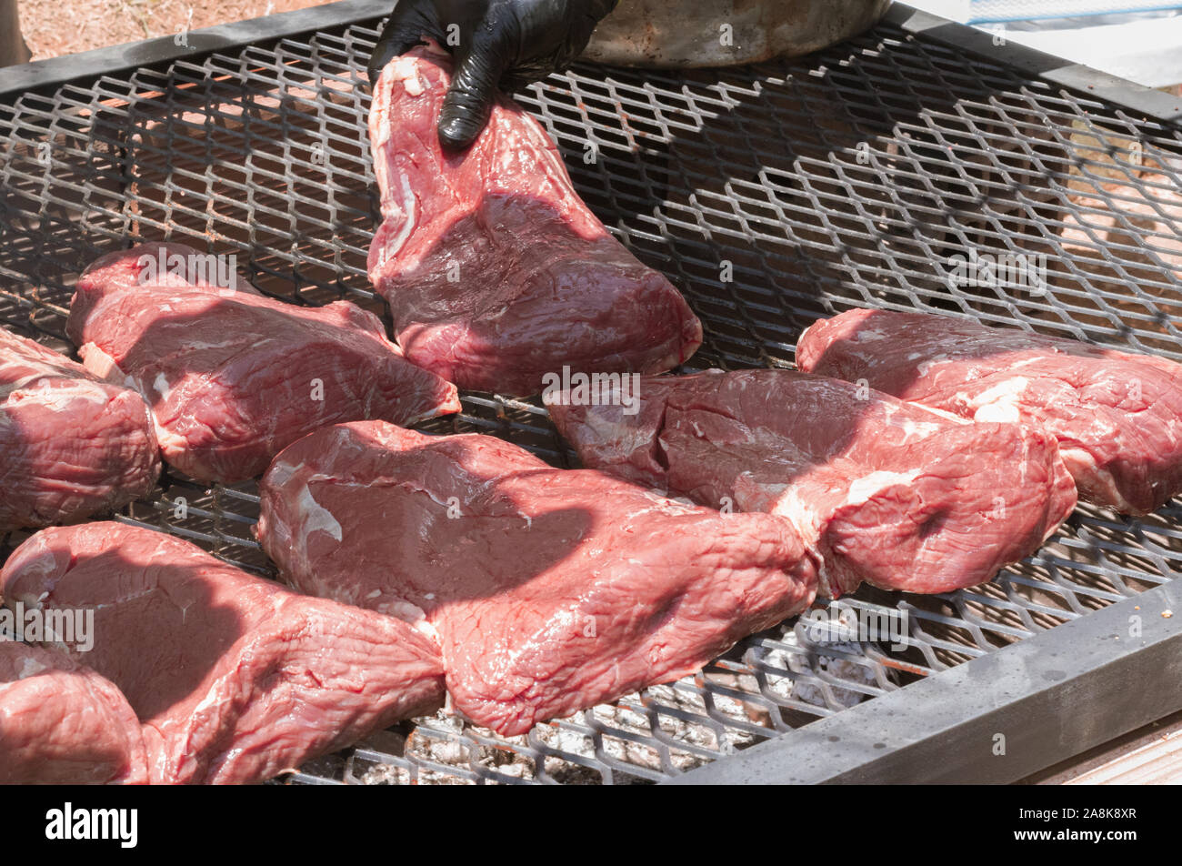 Eine Hand mit einem Picanha, traditionelle brasilianische Barbecue, oben auf einem brennenden Grill in der Sonne Stockfoto