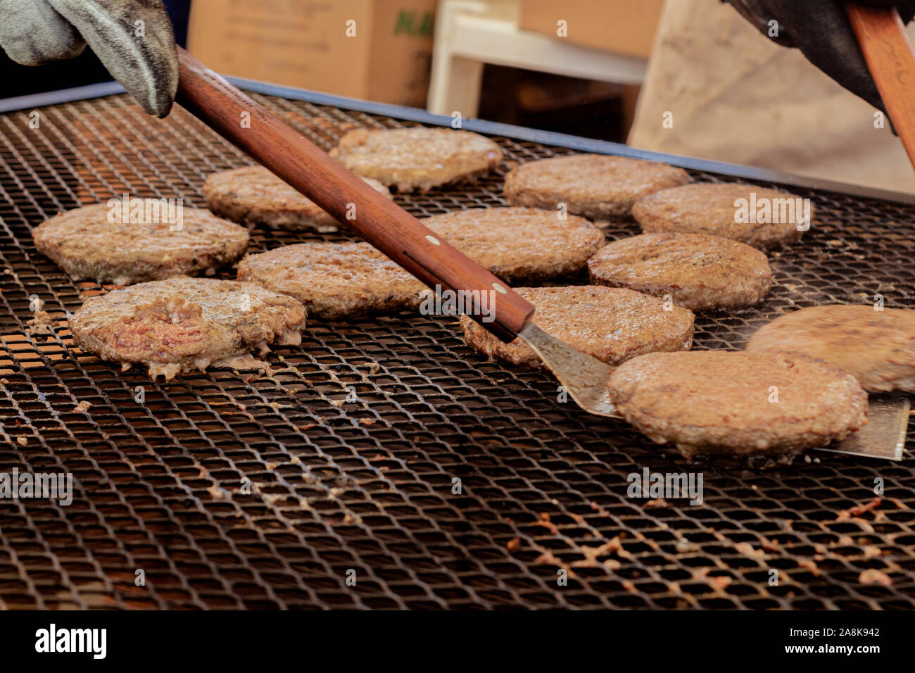 Eine Hand mit einem Spachtel spiegeln einen Burger Fleisch auf dem Grill Stockfoto