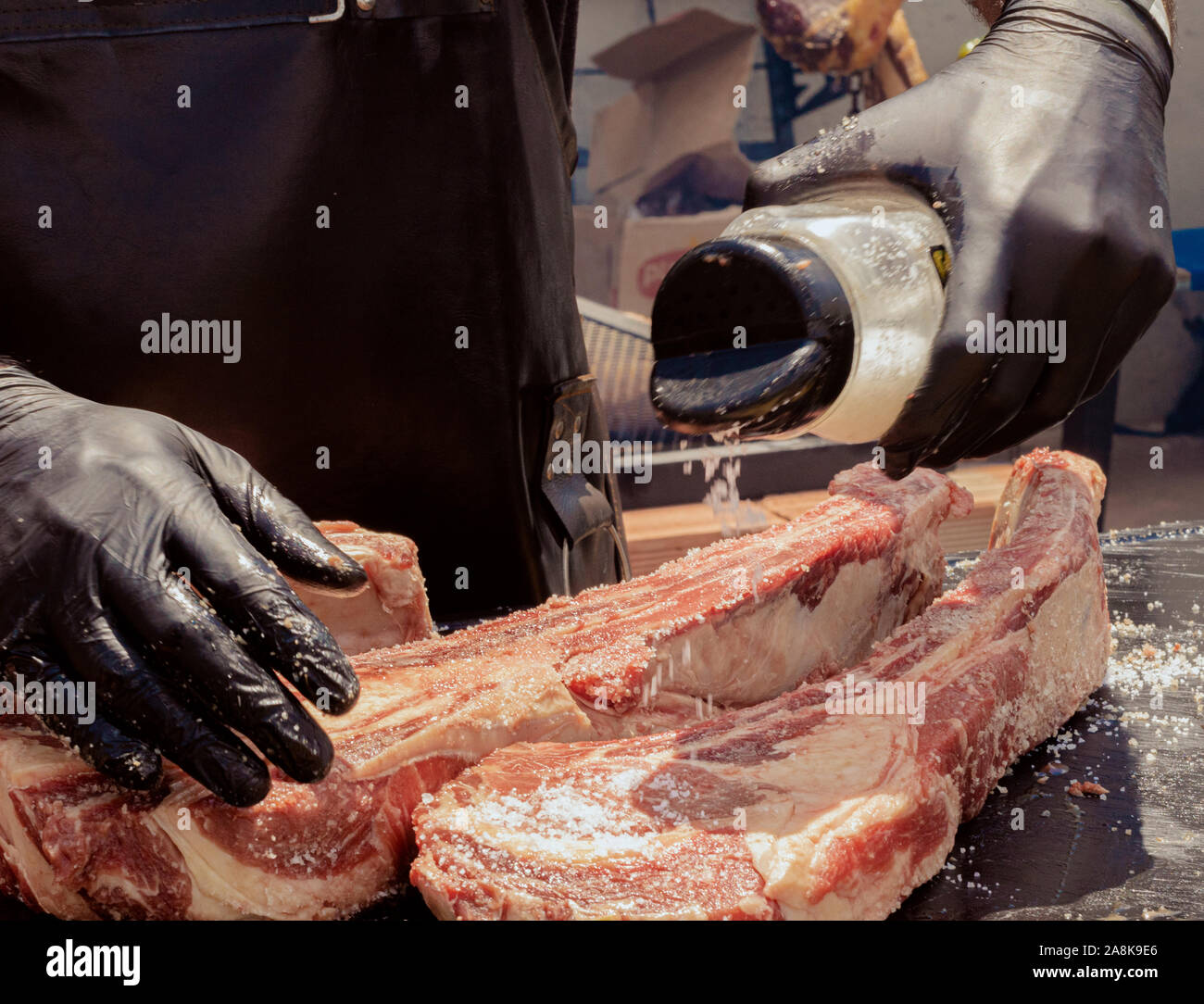 Eine hand salz in ein Stück von Tomahawk Fleisch in der Sonne mit schwarzen Handschuhen Stockfoto