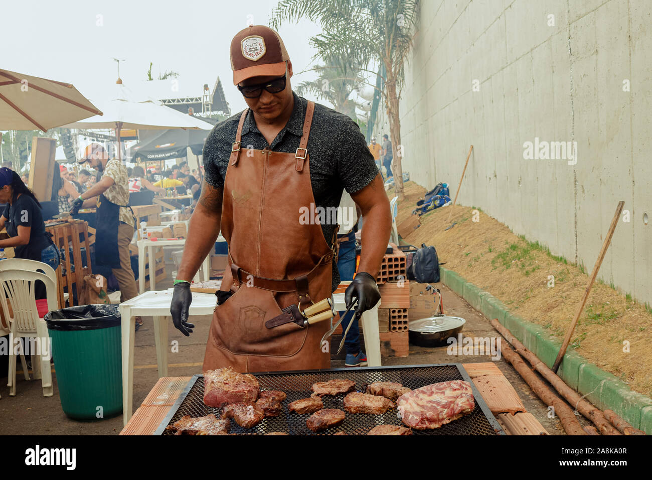 Ein Mann mit Hut und schwarzen Handschuhen drehen um ein Stück Fleisch auf dem Grill Stockfoto