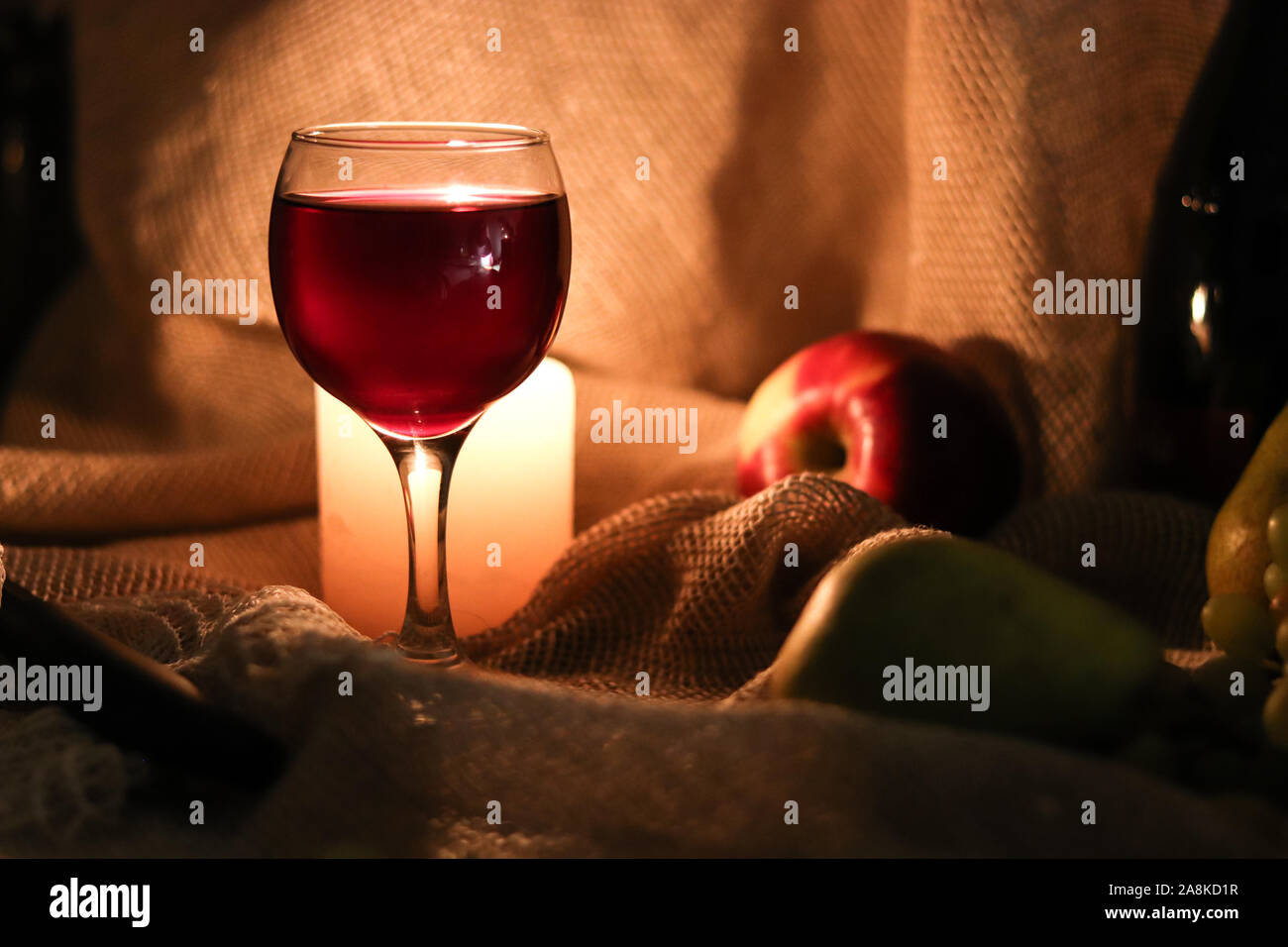 Immer noch leben. Ein Glas Rotwein und Kerzenlicht dahinter auf Tisch in einer halben Licht mit Früchten auf Sack Hintergrund Stockfoto