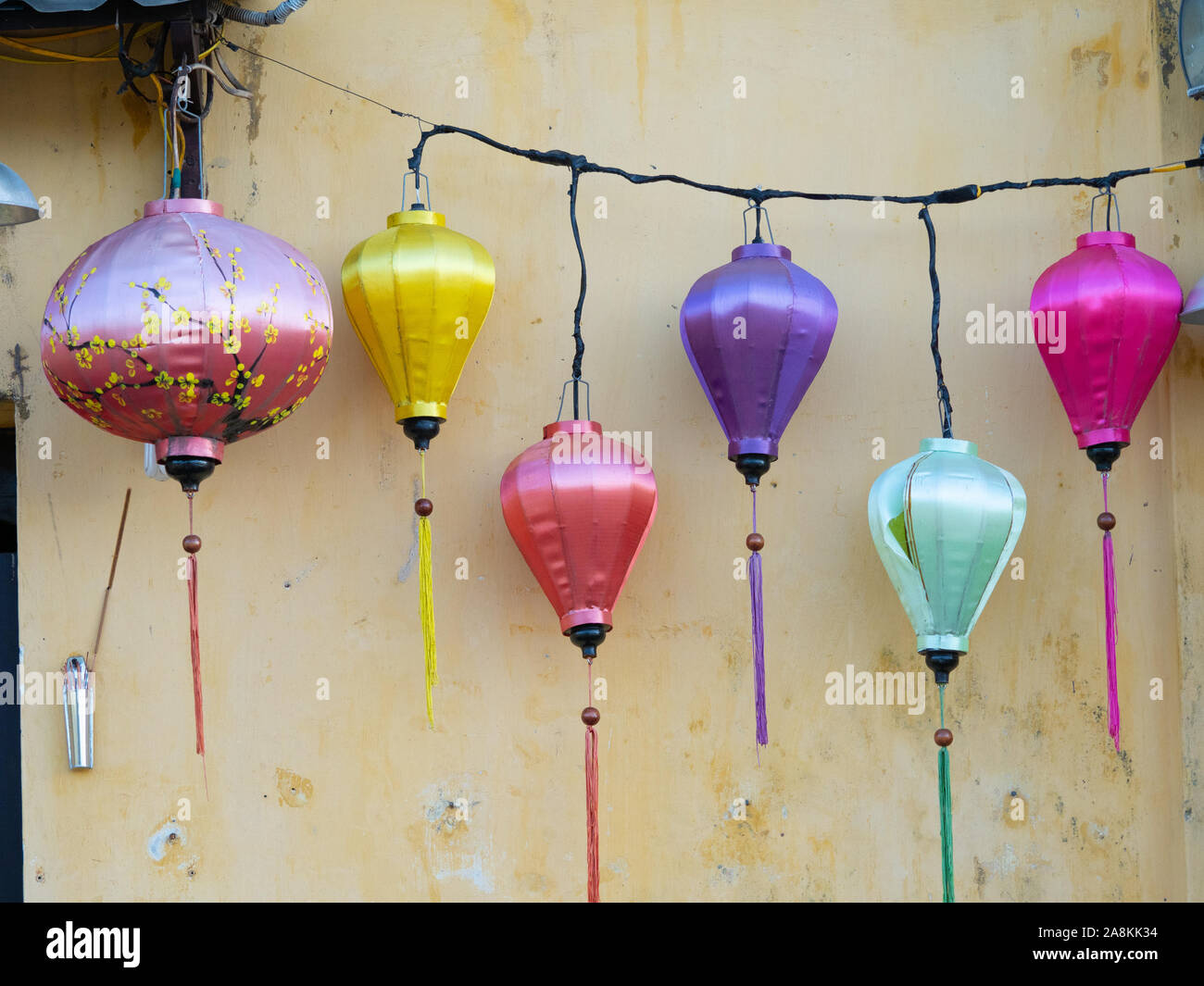 Sechs Satin-qualität Laternen in Pink, Gelb, Lila, und Mintgrün hängenden gegen eine verwitterte, gold Stuckgebäude. Stockfoto