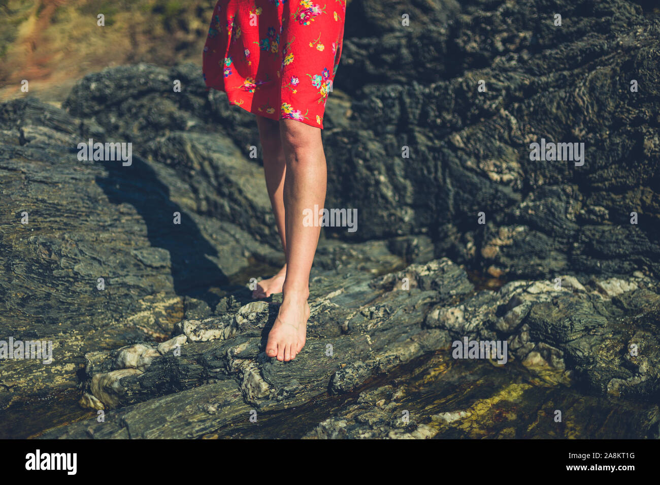 Die Beine und Füße von einer jungen Frau, die zu Fuß auf einem felsigen Strand im Sommer Stockfoto