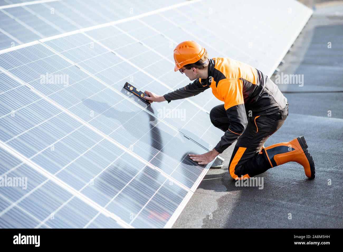 Gut ausgestattete Arbeiter in Schutzkleidung orange Kleidung Installation von Sonnenkollektoren, der Neigungswinkel messen auf eine Photovoltaik Anlage auf dem Dach Stockfoto